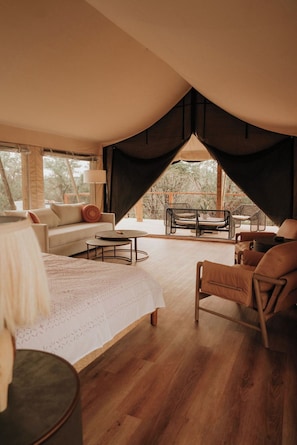 A cozy bedroom with a bed, a sofa, a dining table, and chairs. There is a large window and a view of the outdoors. - Marigold - Luxury Glamping Tent (Johnson City)