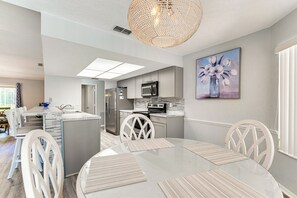 A modern kitchen with a central island, white cabinetry, and a dining area with a round table and white chairs. - 9 Mi to Beach! Poolside Escape in Spring Hill (Spring Hill)