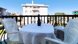 Un balcon avec une table dressée pour deux personnes, deux chaises en plastique blanches et une bouteille de vin.