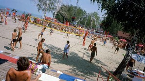 Una cancha de voleibol de playa con jugadores, espectadores y gente disfrutando de la playa.