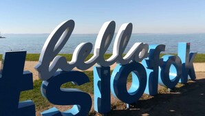 A large outdoor sign with the words "hello" and "Slovak" in a stylized font, placed on a grassy area with a body of water and a clear sky in the background.