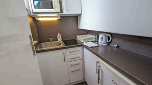 Una cocina compacta con armarios blancos, microondas, hervidor y lavabo.