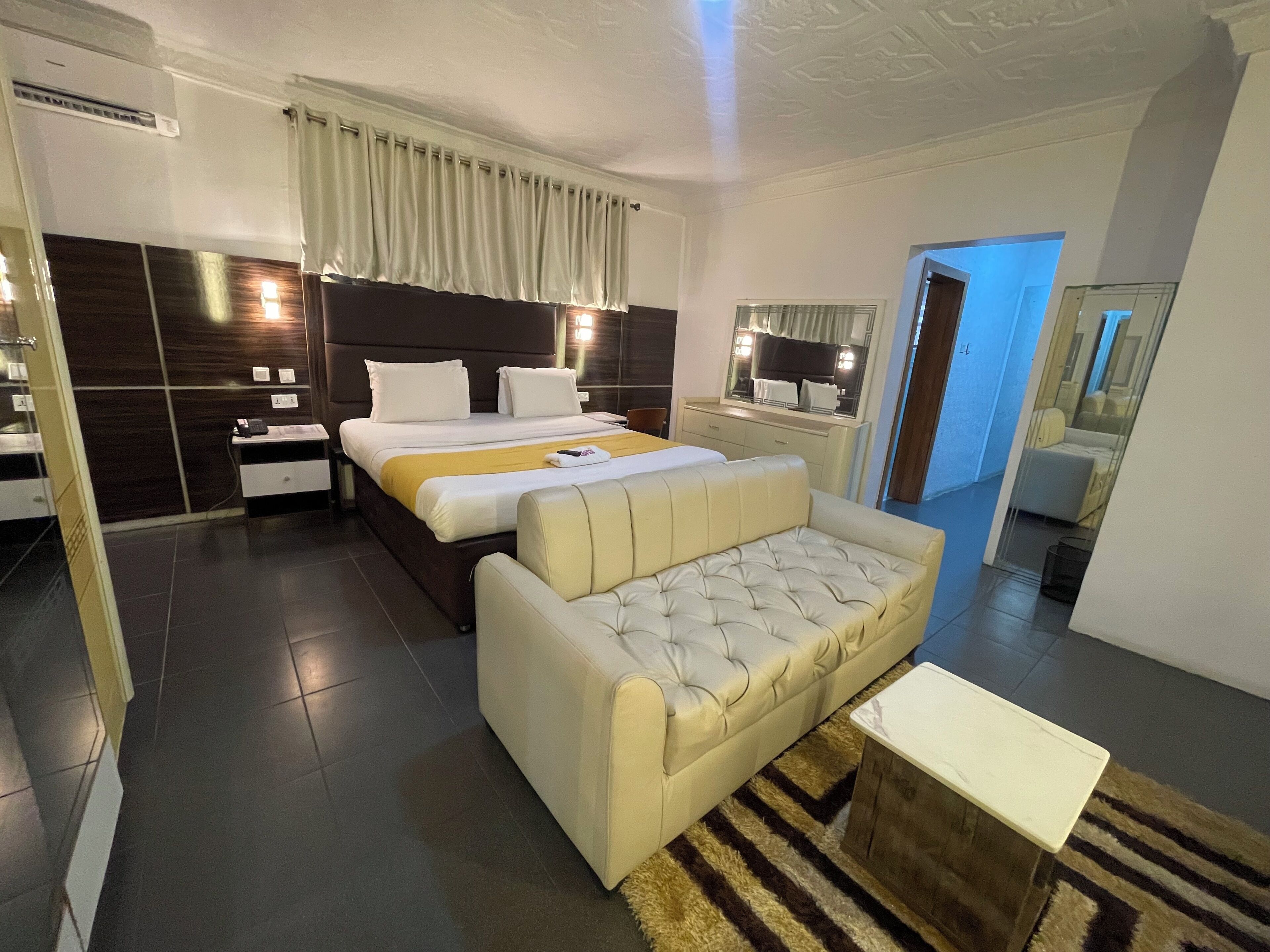 A modern hotel room with a large bed, a sofa, a small table, and a mirror.