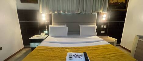A hotel room with a bed, a nightstand, a telephone, a remote control, and a painting on the wall.