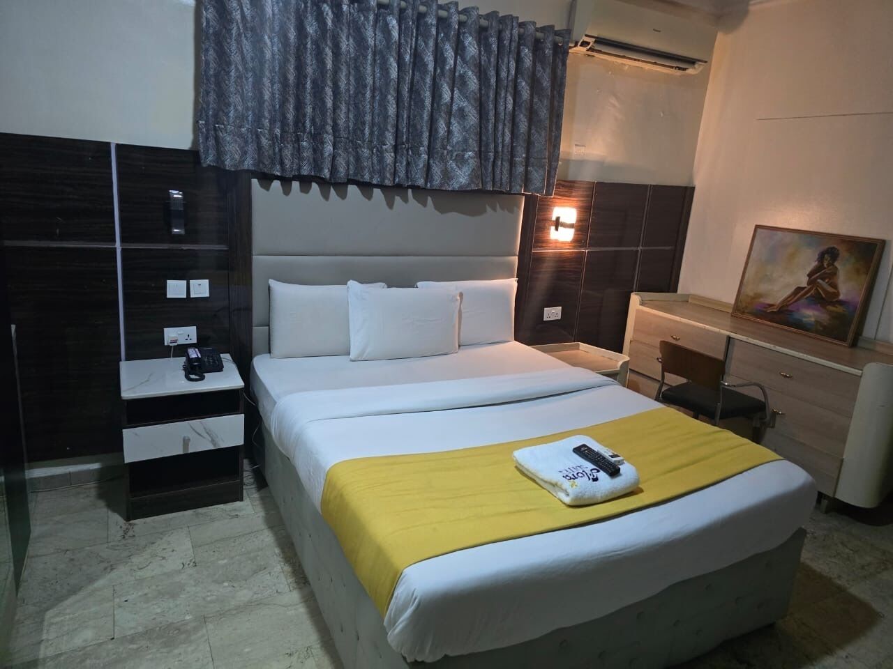 Ein Hotelzimmer mit Bett, Nachttisch, Kommode und einem Bild an der Wand.