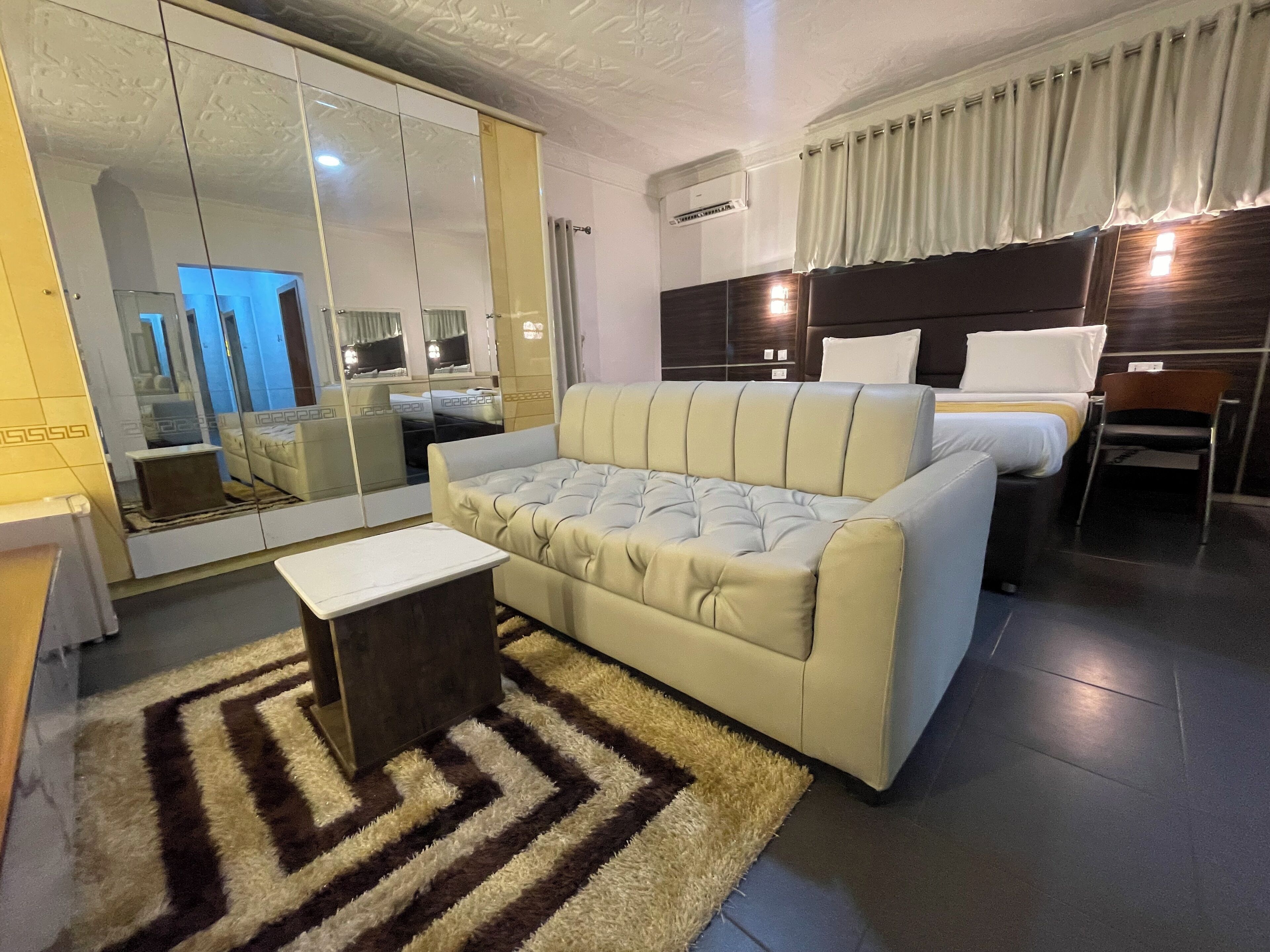 Une chambre d’hôtel moderne avec un grand miroir, un canapé, un lit et une petite table.