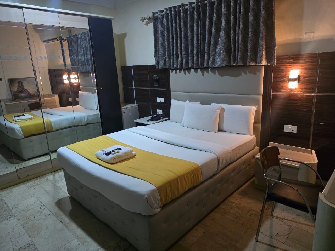 A hotel room with a bed, bedside table, mirror, and a chair.