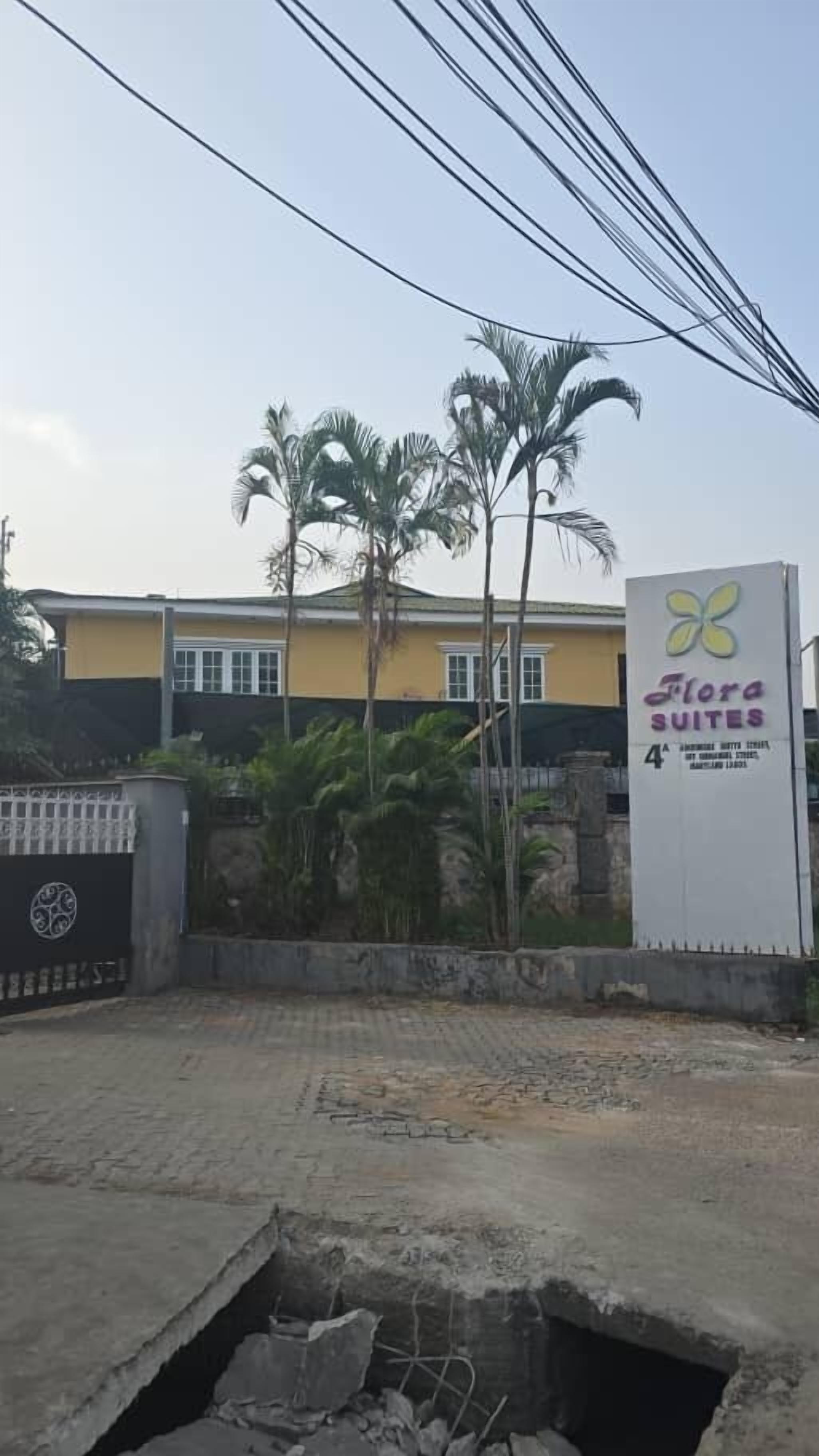 A hotel sign with a logo and name, surrounded by palm trees and a yellow building.