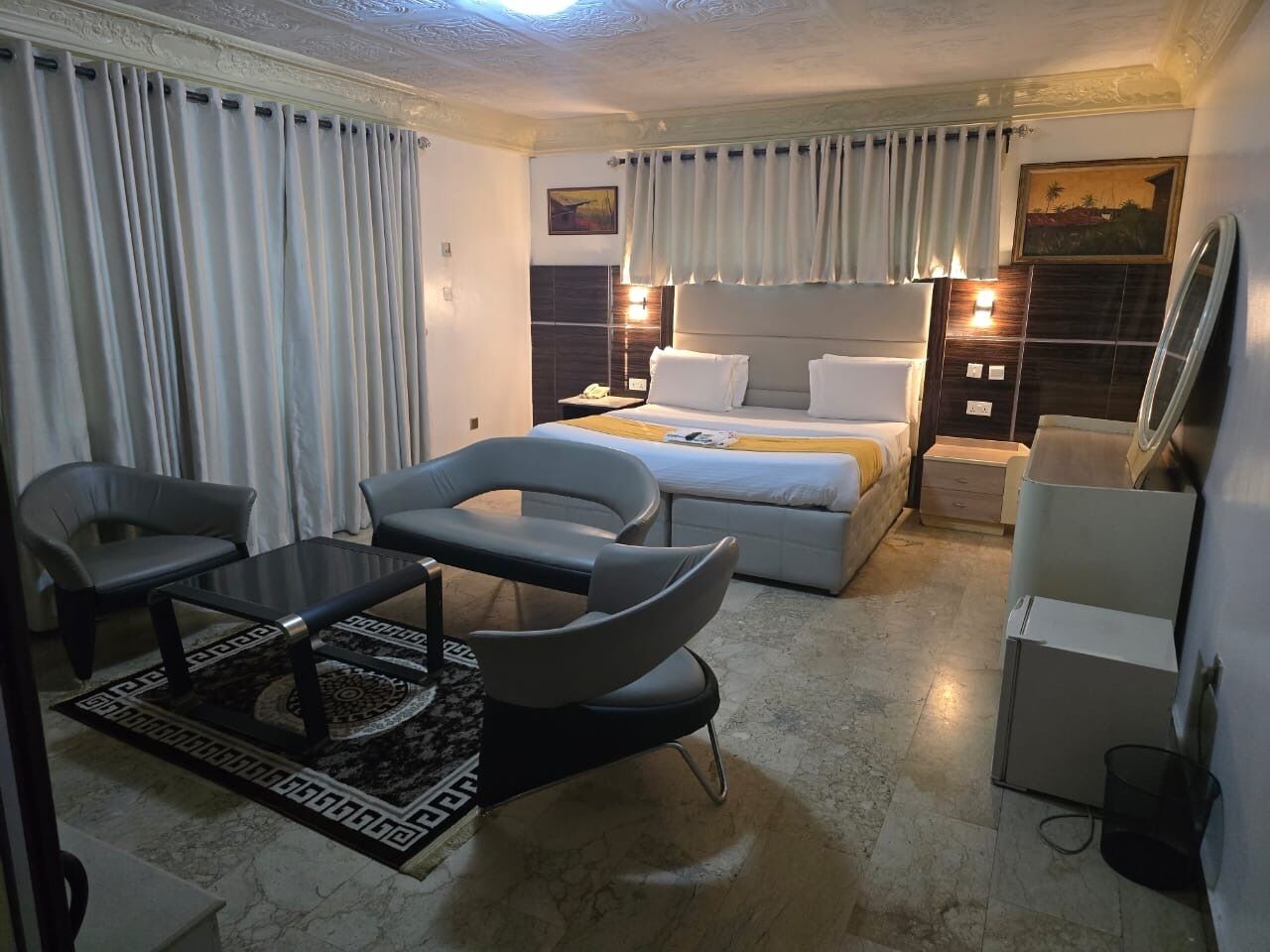Una habitación de hotel moderna con una cama, dos sillones, una mesita, una mesita de noche y un escritorio.