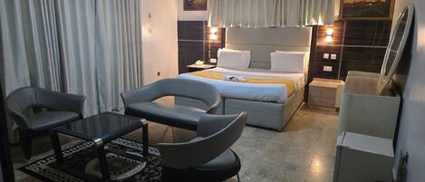 Una habitación de hotel moderna con una cama, dos sillones, una mesita, una mesita de noche y un escritorio.