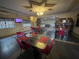 Un comedor de hotel con una mesa de vidrio, sillas rojas, una araña y un televisor en la pared.