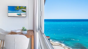 Een balkon met uitzicht op de oceaan, een lijst met een afbeelding van een strand en een tafeltje met een plant.