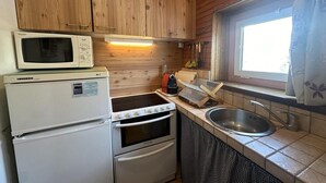 A compact kitchen with wooden cabinets, a microwave, a stove, a sink, and a window with curtains.