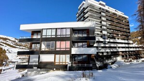 A modern multi-story building with balconies, large windows, and a snowy landscape in the background.