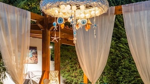 Een terras met rieten meubels, kussens in blauwgroen en een decoratieve hanglamp.