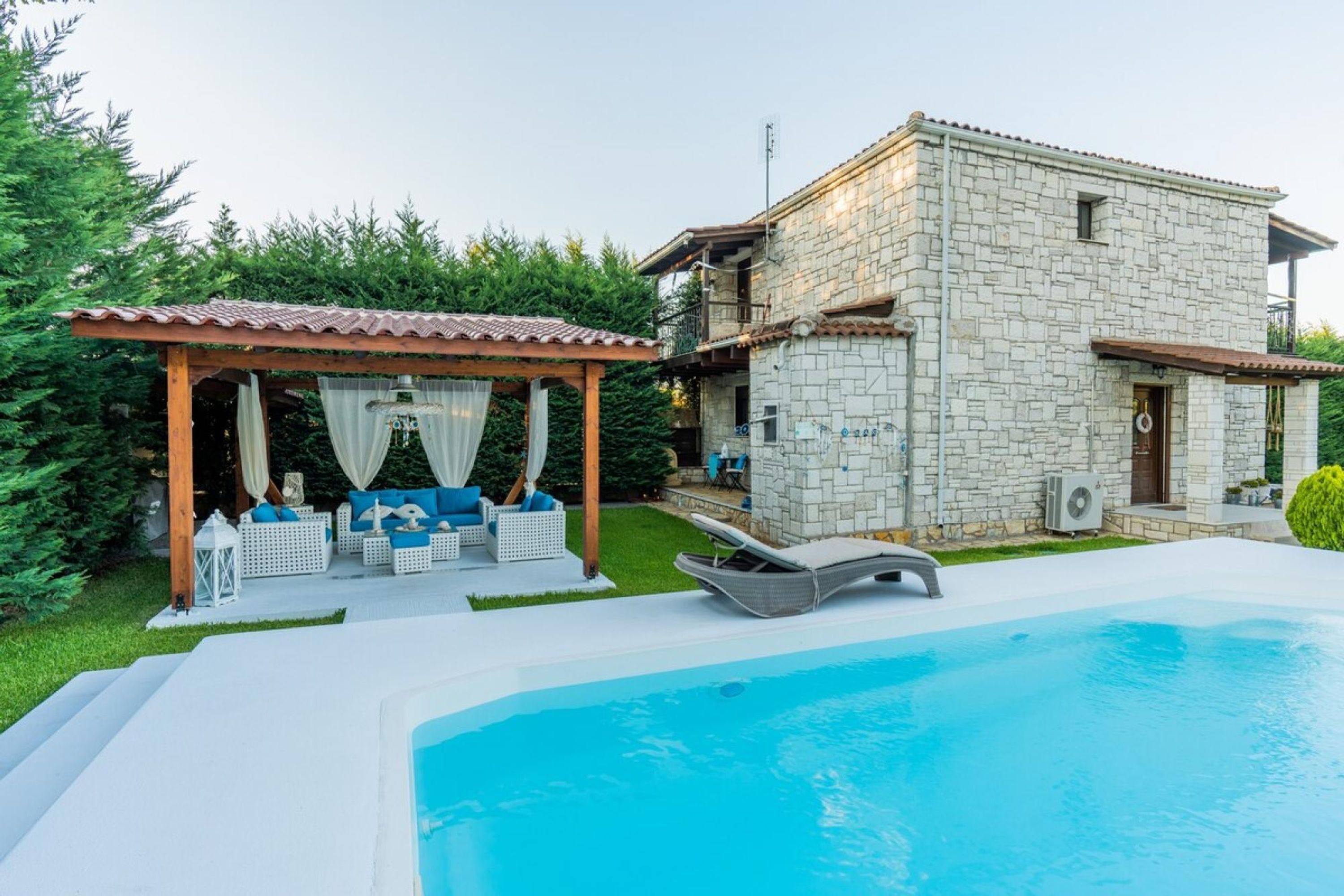 A stone house with a swimming pool, a covered outdoor seating area, and a well-maintained garden.