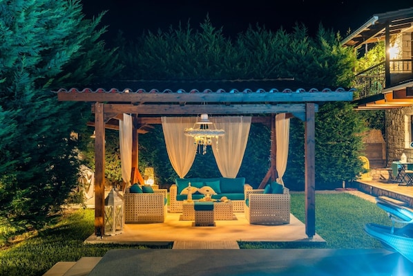 Area esterna con posti a sedere, mobili in vimini, un lampadario e una piscina.