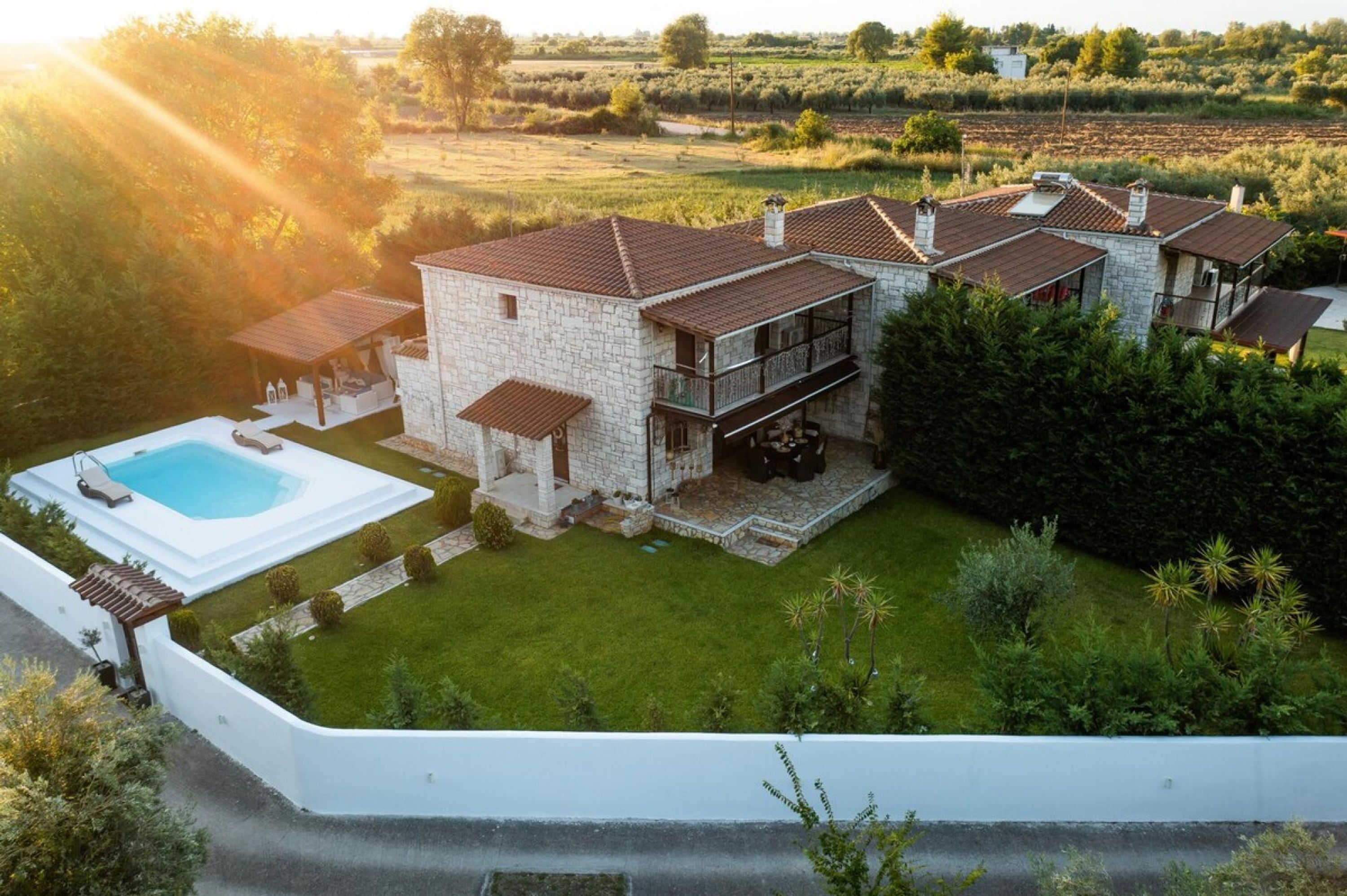 Une maison en pierre avec une piscine, entourée d’une pelouse bien entretenue et d’arbres.