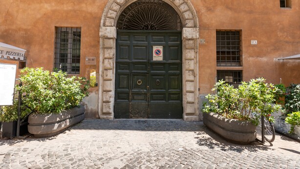 A building with a green door, a sign prohibiting parking, and potted plants. - Apartment with view on Piazza Navona (Rome)
