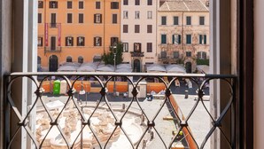 A view through a window with a metal grille, featuring a street scene with buildings and a construction site. - Apartment with view on Piazza Navona (Rome)