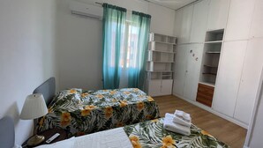 A bedroom with two beds, a wardrobe, and a window with curtains.