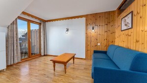 Une pièce avec un plancher en bois, un canapé bleu, une table en bois et une porte-fenêtre coulissante donnant sur un espace extérieur.
