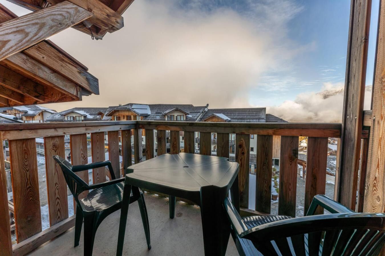 Een houten terras met een tafel en stoelen, met uitzicht op een rij huizen.