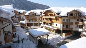 Une station de ski enneigée, avec des bâtiments en bois, des balcons et une vue dégagée sur les montagnes en arrière-plan.