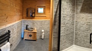 A wooden cabin bathroom with a stone wall, a wooden sink with a basin, and a small window above the mirror. - Pet Friendly - Lodge at Riverview Holiday Park (Newcastleton)