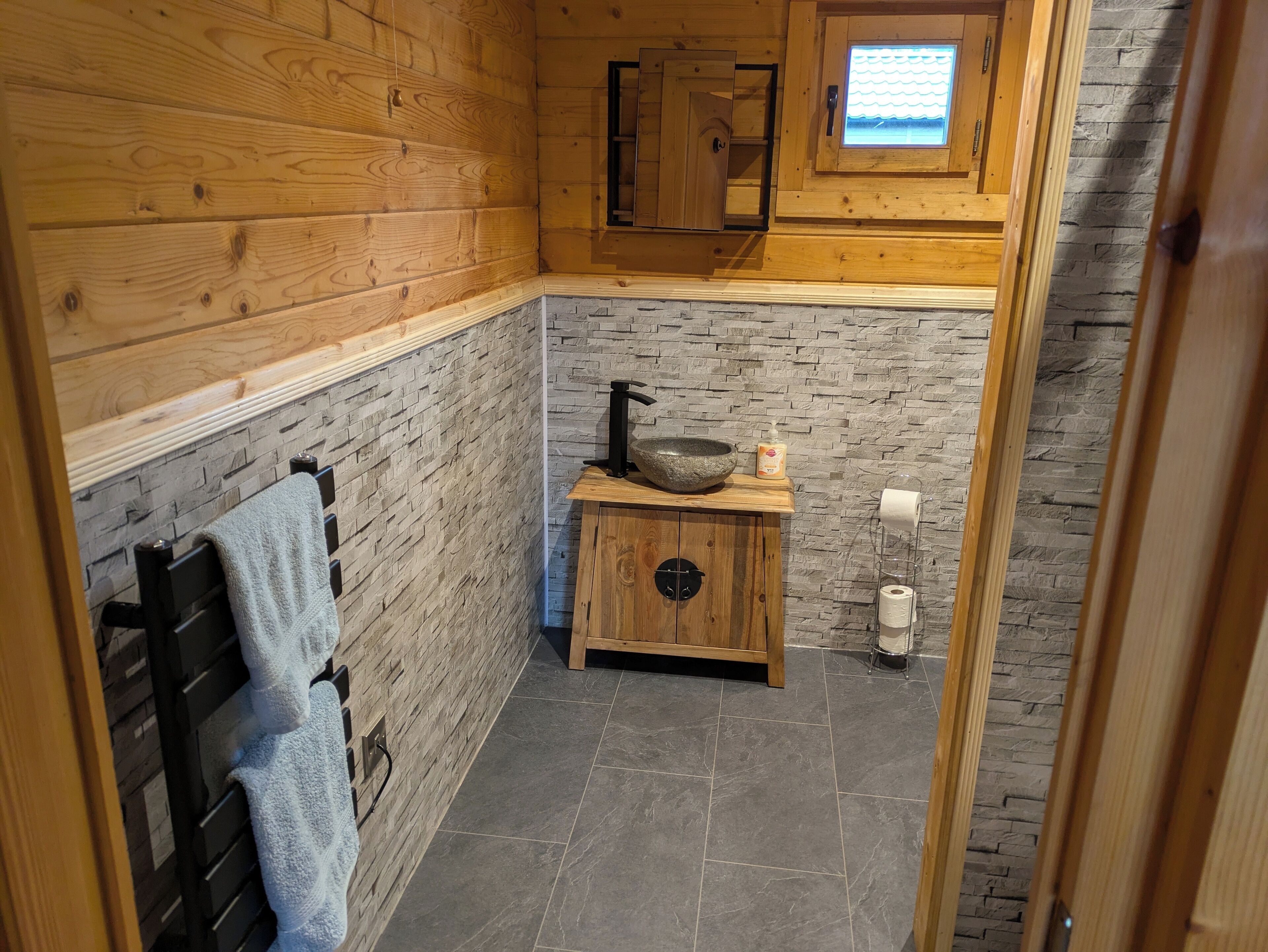 Un baño pequeño con paredes de madera, un salpicadero de piedra, un mueble de madera con lavamanos y un perchero.