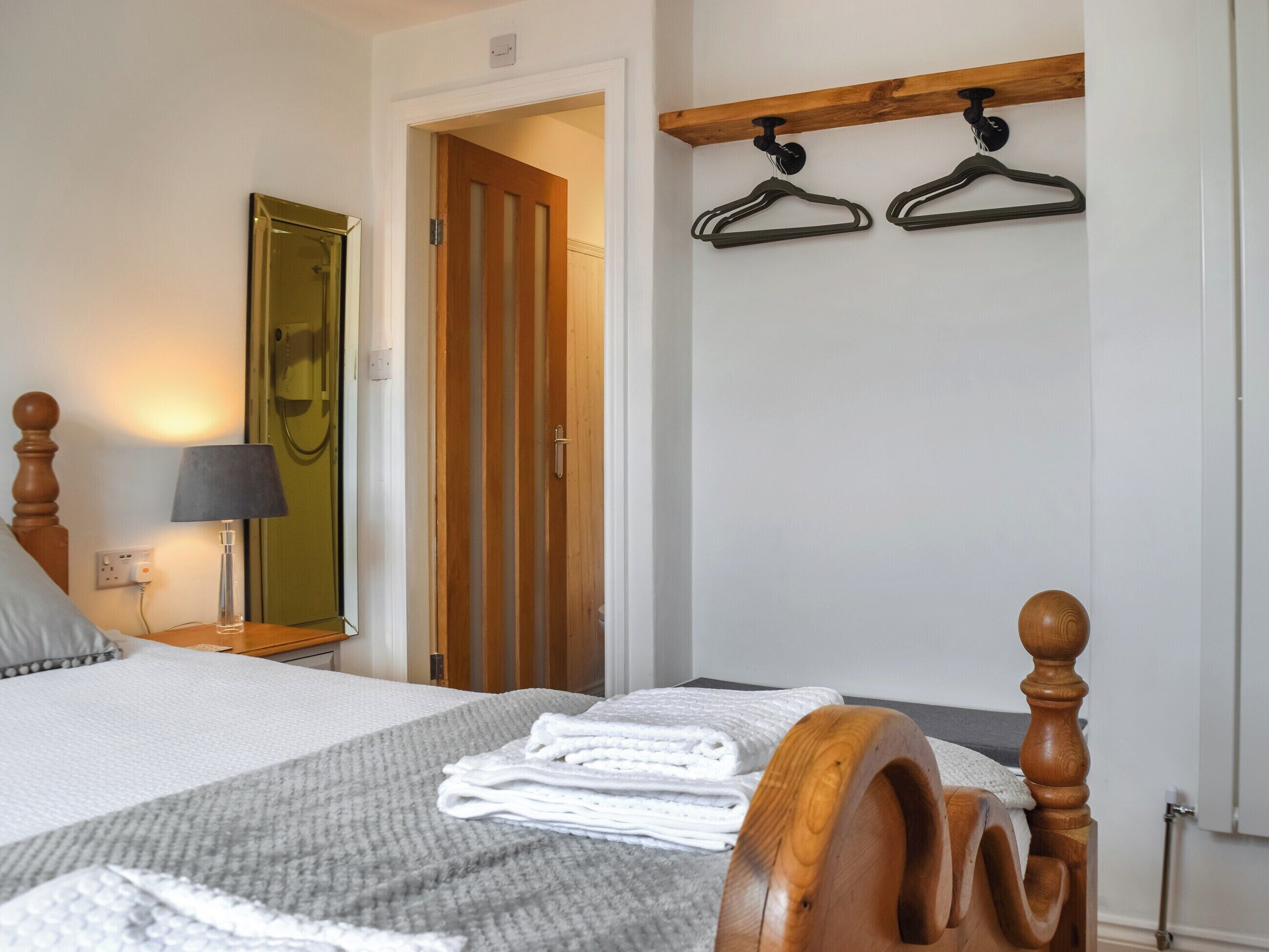 Habitación de hotel con una cama, cabecera de madera, mesita de noche con lámpara, espejo y una puerta que da a otra habitación.