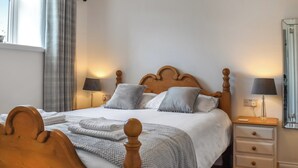 Un lit bien fait, avec une tête de lit en bois, deux lampes de chevet et une table de chevet dotée d’un miroir.