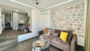 A modern living room with a stone wall, a brown sofa, a glass coffee table, and a kitchen in the background. - Villa Vojnic (Kuljace)