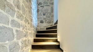 A staircase with stone walls and wooden steps, illuminated by wall-mounted lights. - Villa Vojnic (Kuljace)