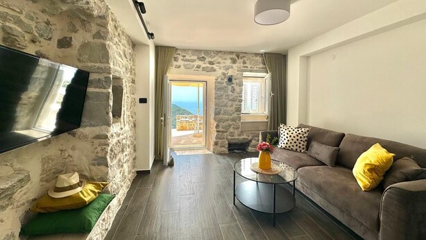 A living room with a stone wall, a flat-screen TV mounted on the wall, a sofa with yellow and black cushions, and a coffee table with a vase. - Villa Vojnic (Kuljace)