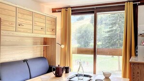 Una stanza accogliente con un tavolo di legno, sedie, un divano blu e un'ampia finestra con tende.