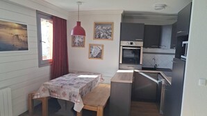 Una cocina compacta con comedor, piso de madera y una lámpara colgante roja.