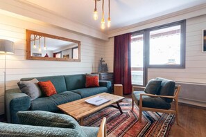 A cozy living room with a green sofa, a wooden coffee table, and a patterned rug. - 100m from ski slopes, 1st floor, swimming pool, sauna, hammam, balcony, fireplace or stove, tv (Val Thorens)