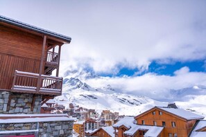 A wooden building with a balcony, a stone base, and a snowy mountain backdrop. - 100m from ski slopes, 1st floor, swimming pool, sauna, hammam, balcony, fireplace or stove, tv (Val Thorens)