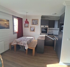 A compact kitchen with a dining area, wooden flooring, and a red pendant light.