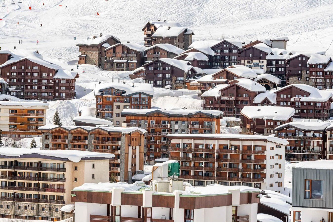 Et snedækket feriested med flere bygninger, herunder hytter og lejligheder, og ski slopes i baggrunden.