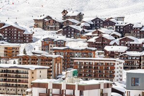 A snow-covered resort with multiple buildings, including lodges and apartments, with ski slopes in the background.
