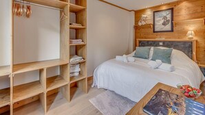 A bedroom with a wooden wardrobe, a bed with white bedding, a small table with a book and a bowl of fruit, and a framed picture on the wall. - 1st floor, tv, ski locker, 50m², Tignes (Tignes)