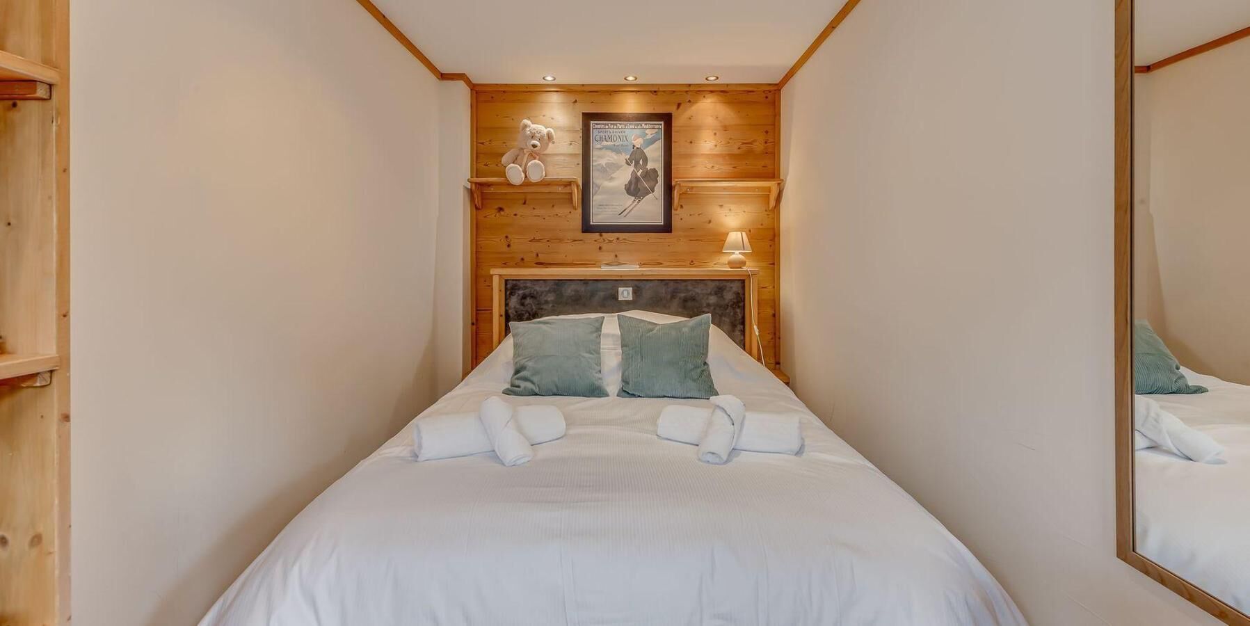 Een kleine kamer met een bed, houten wanden, een lijst met een afbeelding en een spiegel.