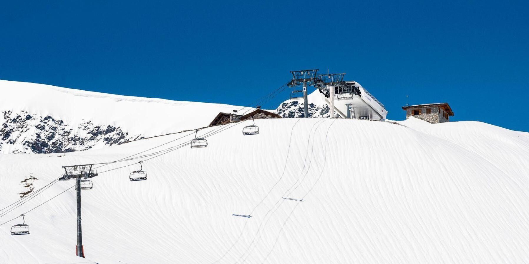 A ski lift on a snowy mountain slope with a clear blue sky.