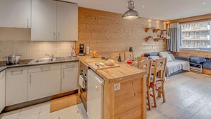 A modern kitchen with a wooden island, a dining area with a sofa, and a view of a building through large windows. - 1st floor, tv, ski locker, 50m², Tignes (Tignes)