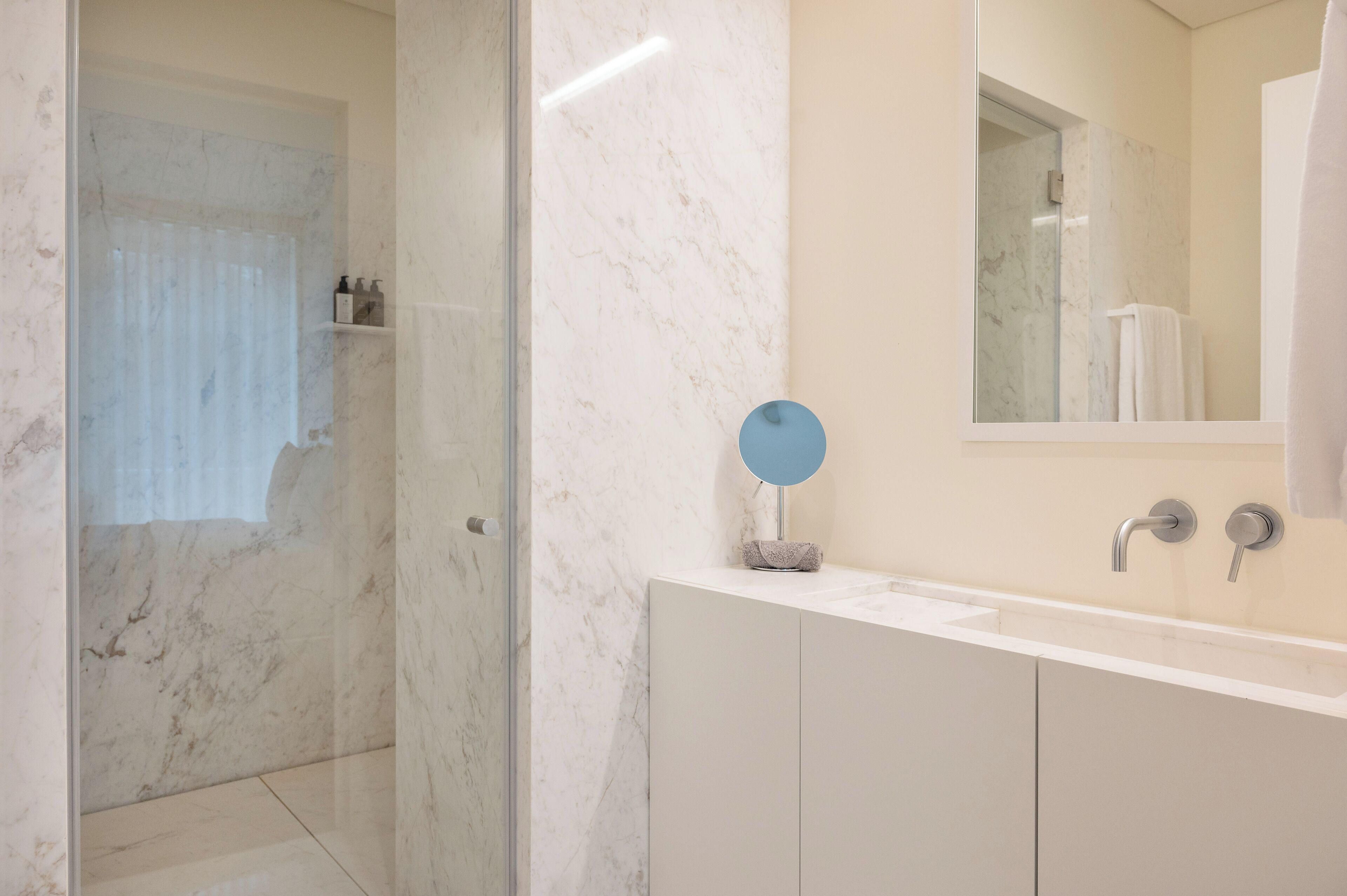 A modern bathroom with a marble shower, a white sink with a mirror, and a glass-enclosed shower area.