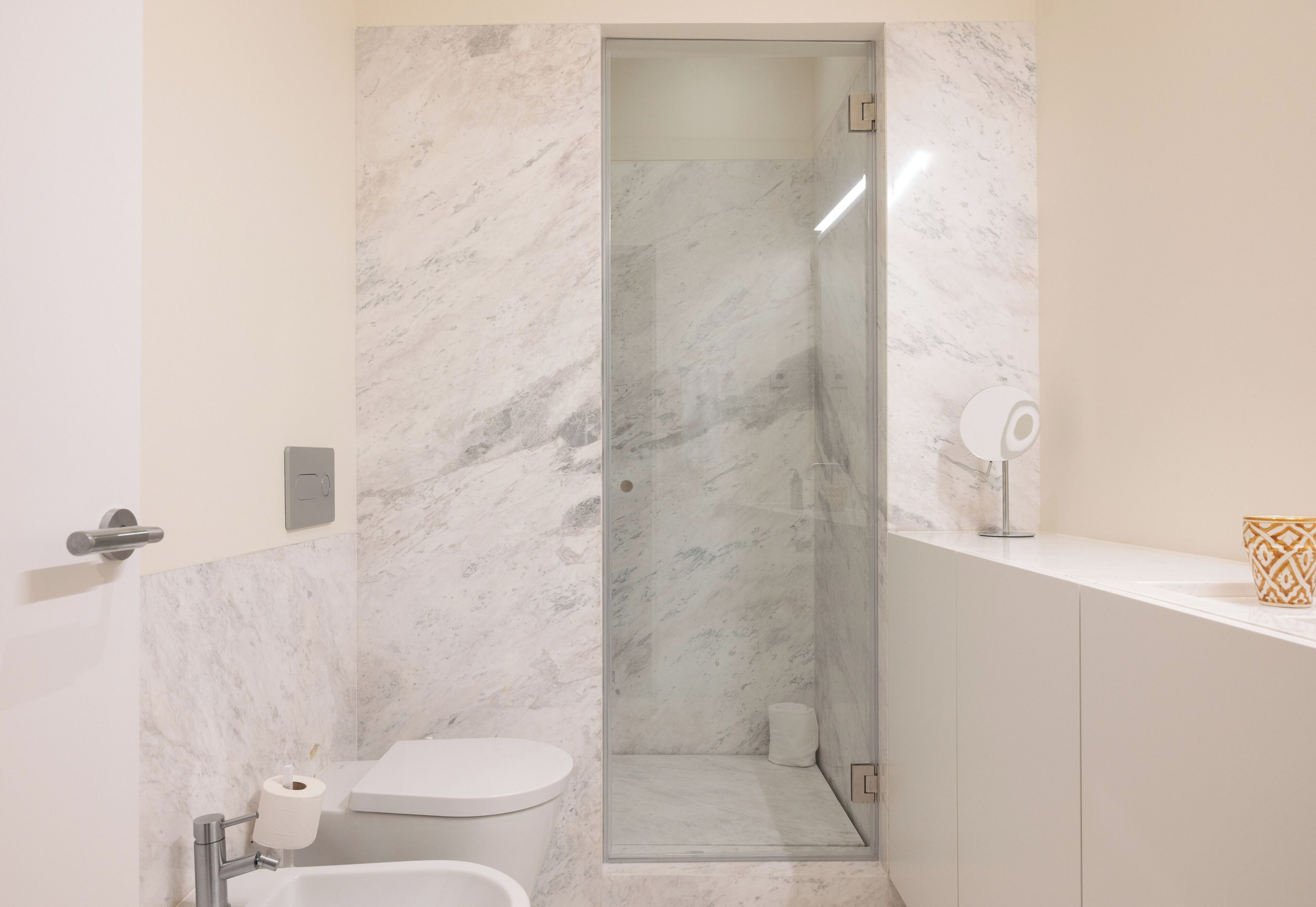 A bathroom with a marble shower, a toilet, and a sink.
