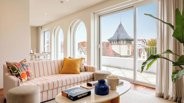 Una sala de estar moderna con un sofá, una mesa de centro y vistas a un paisaje urbano a través de grandes ventanales.