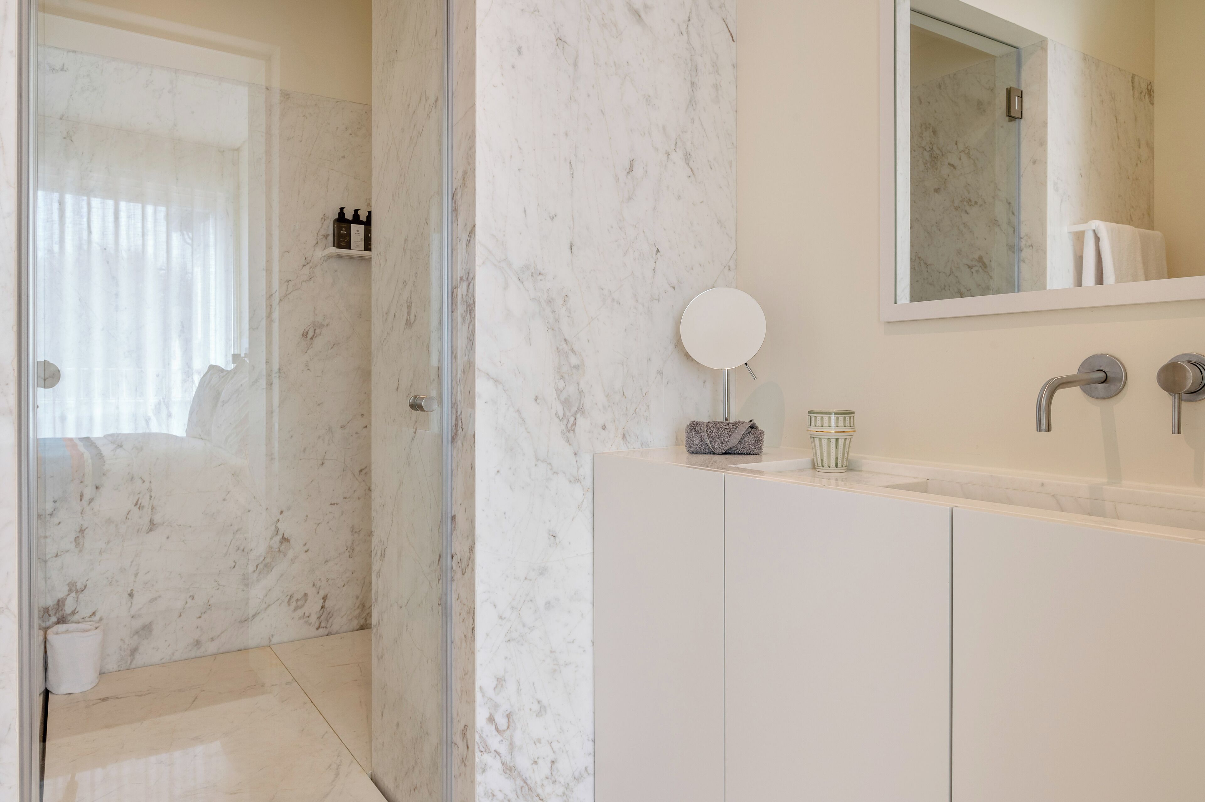 Un bagno moderno con doccia in marmo, uno specchio grande e un mobile lavabo bianco.
